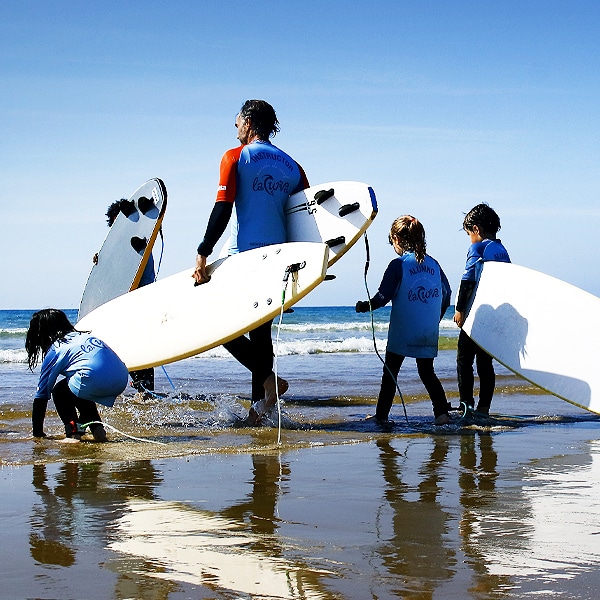 instructor con grupo de niños acercandose al agua para surfear