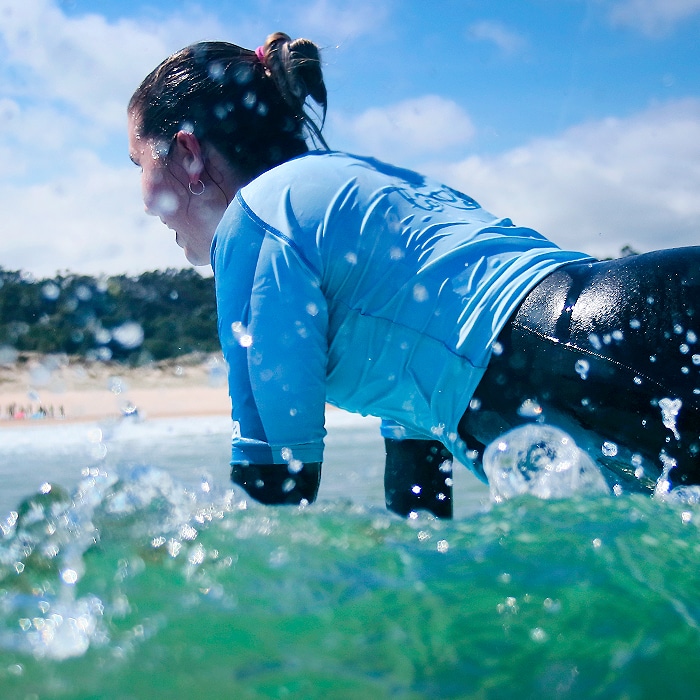 alumna cogiendo una ola durante clase de surf