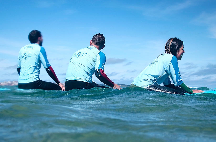 Grupo de alumnos de la escuela en el agua encima de sus tablas durante la clase de surf esperando a la ola y riendo