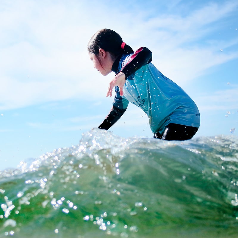 Nina menor en surf camp diurno cogiendo una ola